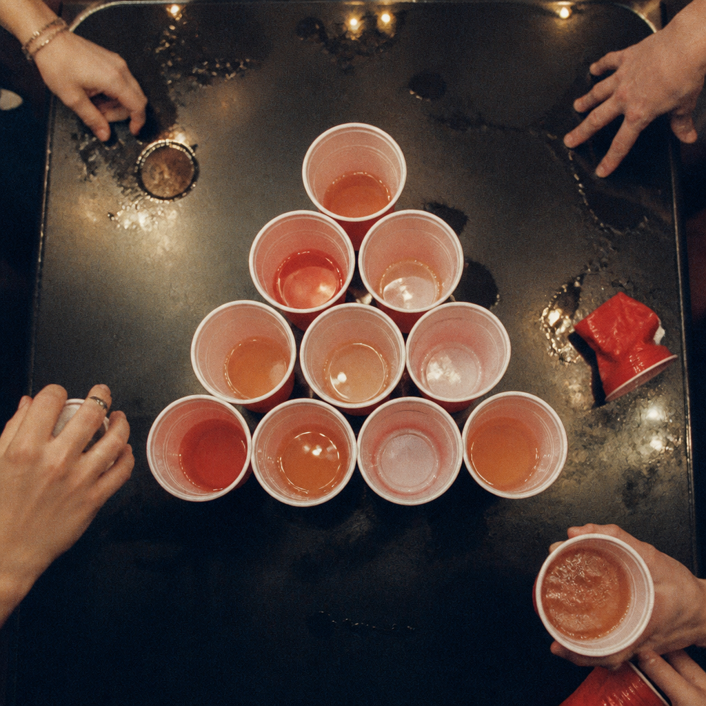 Hands around a pyramid of cups on a beer pong table, seen from above